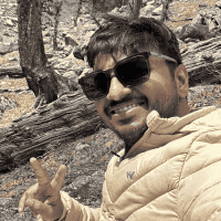 Deven, smiling in sunglasses with a peace sign, on a mountain trail